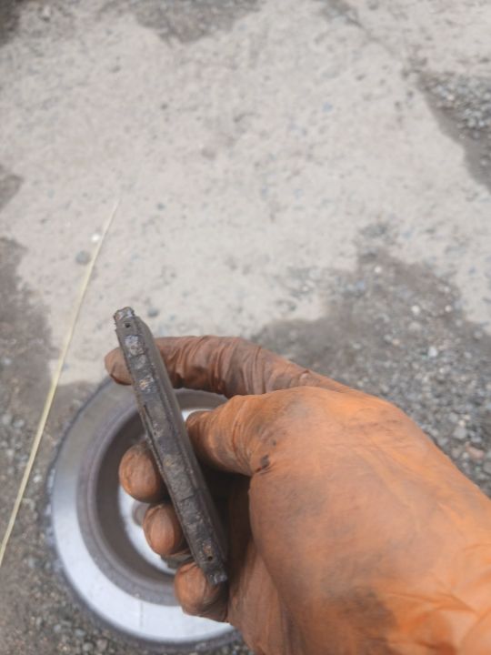 A worn brake pad held in a gloved hand over the brake disc during an on-site brake inspection